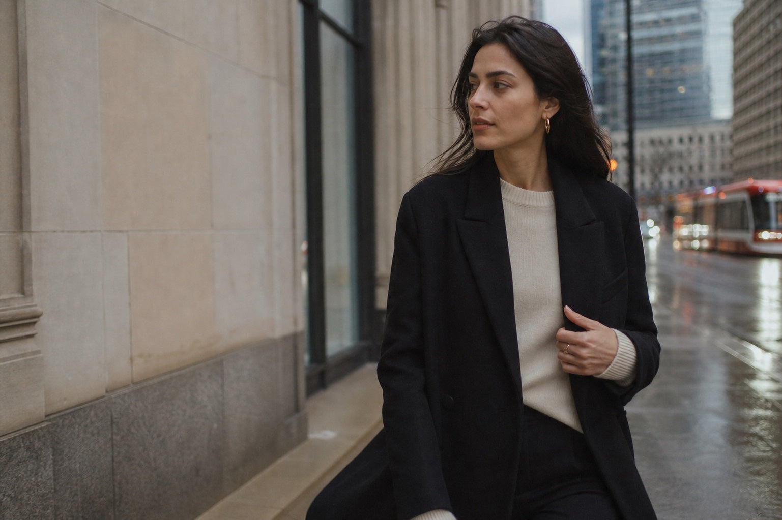 Woman in tailored black outerwear walking through downtown Toronto after rain